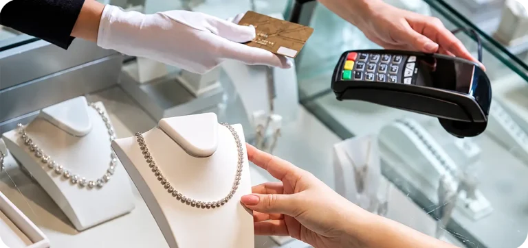 Jewelry store employee processing a customer payment with a POS terminal beside a diamond necklace display.